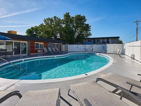 A swimming pool surrounded by a white fence and lounge chairs.