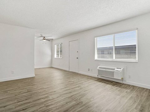 A room with a window, a fan, and a wall-mounted air conditioner unit.
