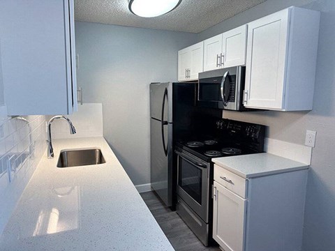 A kitchen with a black fridge, white cabinets, and a white countertop.