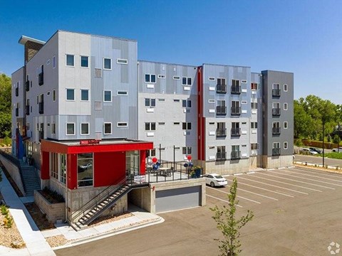 A modern apartment complex with a red awning and a parking lot in front.