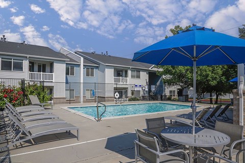 A blue umbrella is next to a table and chairs by a pool.