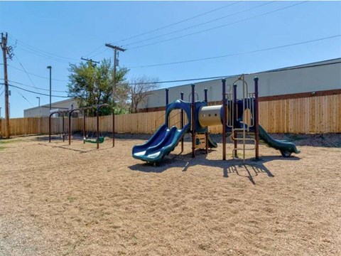 A playground with a green slide and a wooden fence.