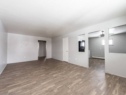 A room with wooden flooring and a white wall with a doorway leading to another room.