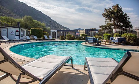 A pool with sun loungers and a mountain in the background.