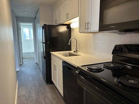 A black refrigerator is in a kitchen with white cabinets.