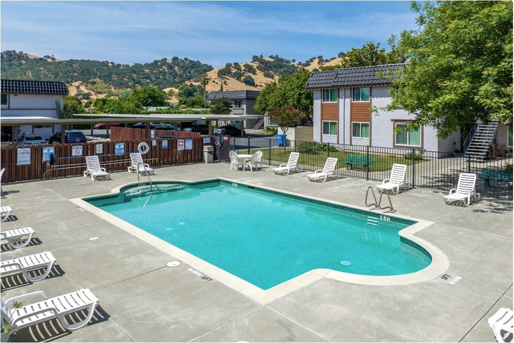 A large swimming pool surrounded by lounge chairs and a hillside in the background.