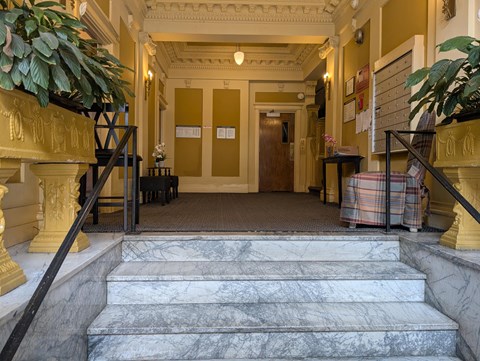 A hallway with a marble staircase and a plant on the left.