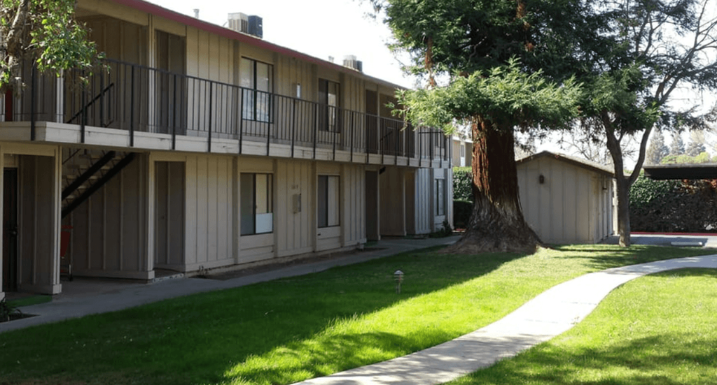 a walkway leading to an apartment building with a large tree in the background