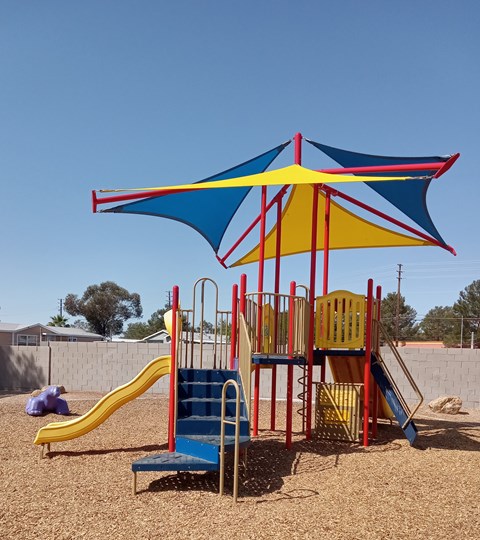 A playground with a blue and yellow umbrella and a yellow slide.