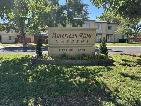 A sign for American River Gardens stands in front of a building.