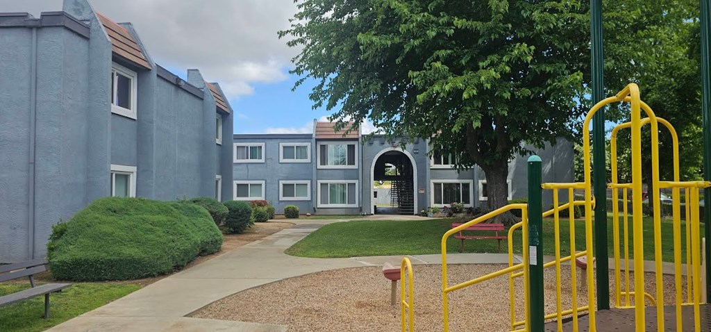A playground with a yellow slide in front of a grey building.
