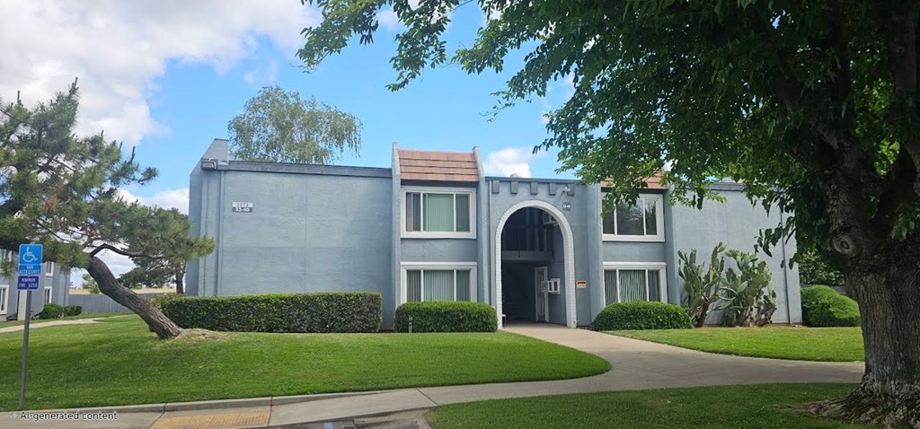 A grey building with a brown roof and a tree in front.