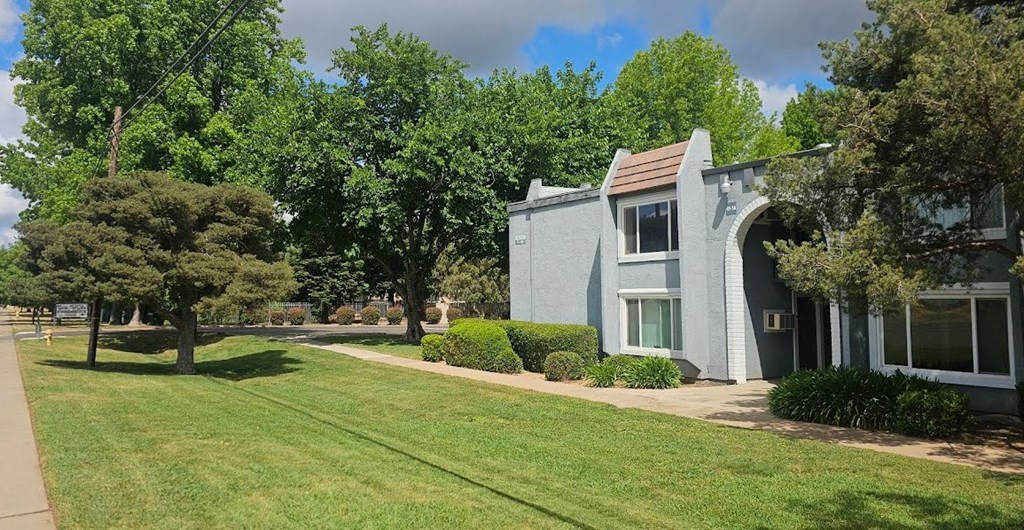 A grey multifamily housing building with a green lawn in front.