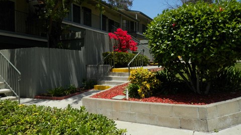 A concrete planter with red flowers in front of a grey house.