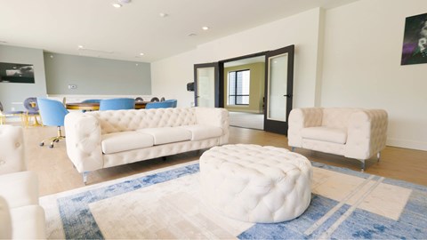 A white tufted ottoman sits in the middle of a blue rug in a living room.