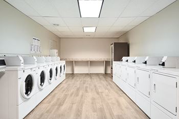 a washer and dryer room with a row of washing machines and dryers