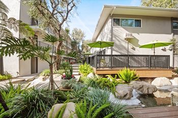 A patio with a table and chairs is surrounded by green plants and trees at Villa Vicente, Los Angeles, CA, 90019