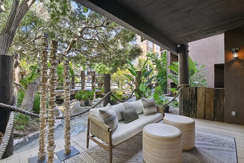 A wooden sofa with cushions sits on a rug in a room with a wooden ceiling and a tree trunk on the left.