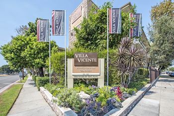 A sign for Villa Vigente is surrounded by plants and flags.