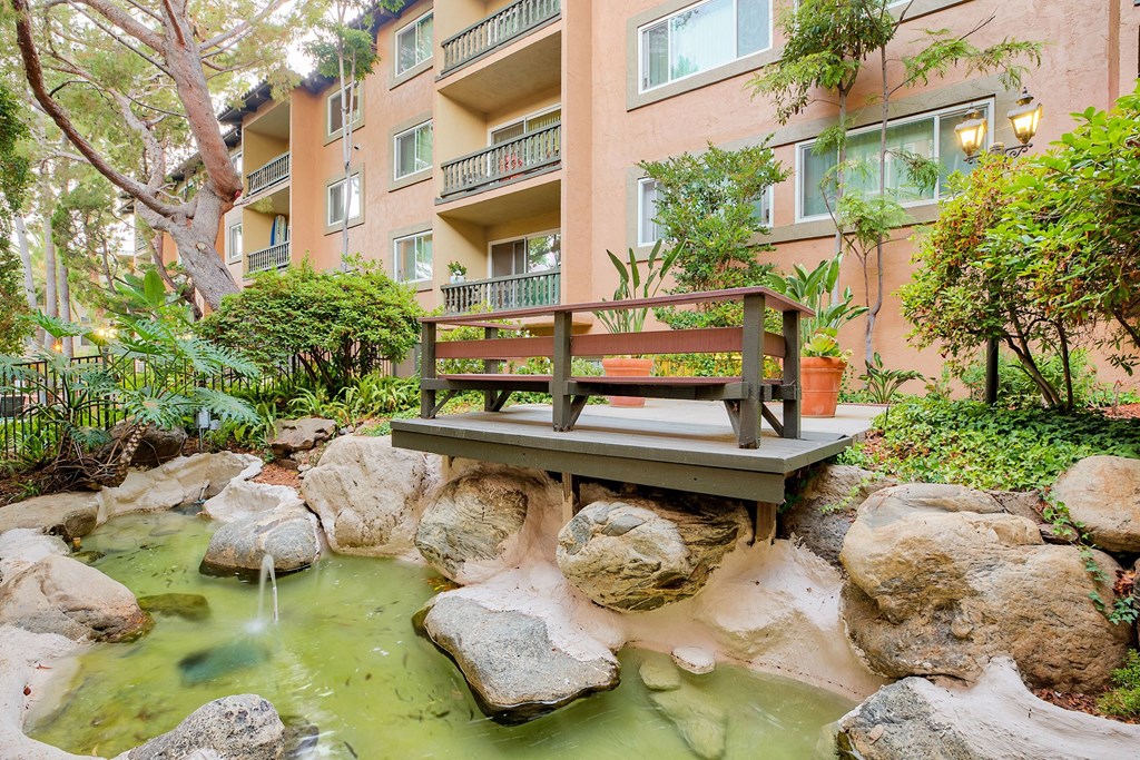a bench sits on a bridge over a stream in front of an apartment building at Casa Granada, Los Angeles, CA