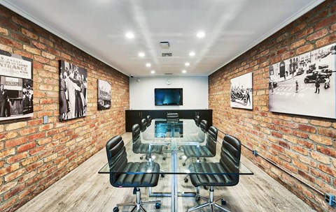 a conference room with a glass table and chairs and an exposed brick wall at The Meadows Apartments, Culver City , CA
