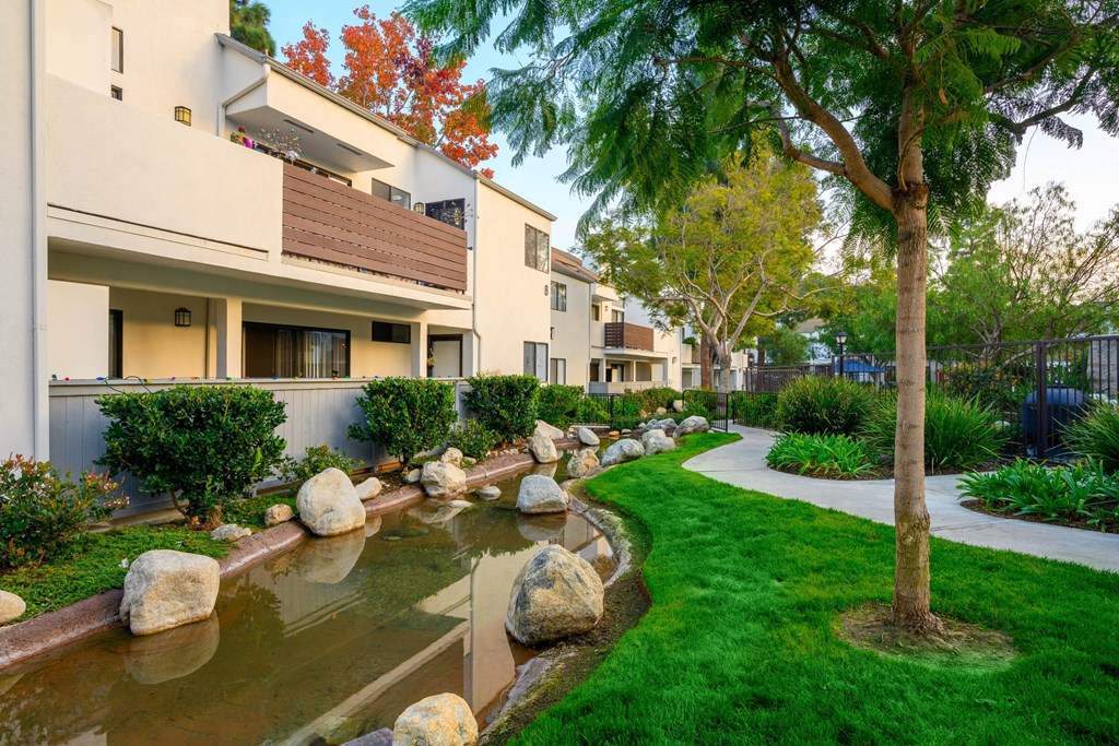 a building with a stream and rocks in the grass