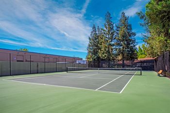 A tennis court surrounded by a fence and trees at Valley Plaza Villages, Pleasanton, California