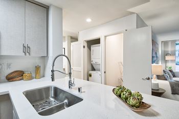A modern kitchen with a stainless steel sink and a wooden cutting board with artichokes on it.