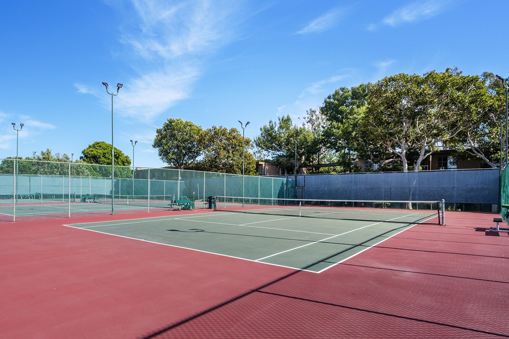 A tennis court with a red surface and green boundary wall at Mariners Village, Marina del Rey, 90292
