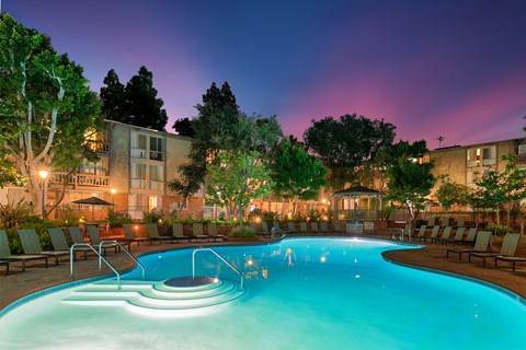 A swimming pool with a few people in it at night.