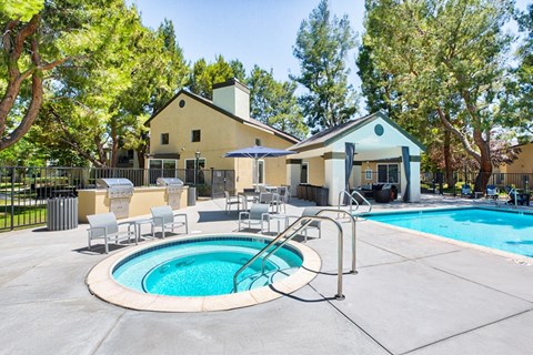 A pool with a hot tub and a house in the background.