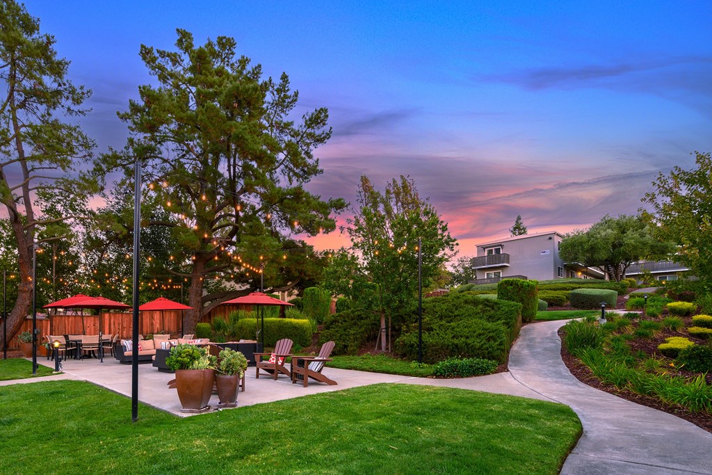 A beautiful outdoor seating area with tables and chairs surrounded by greenery and trees.