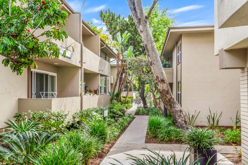 A row of beige apartment buildings with green plants in front at West Park Village, Los Angeles, CA