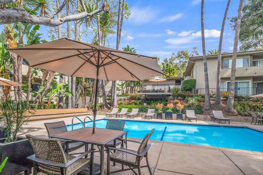 A patio with a table and chairs under an umbrella next to a pool at West Park Village, Los Angeles, CA