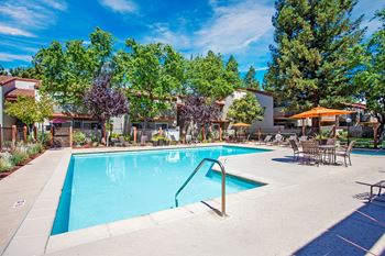 A swimming pool surrounded by trees and chairs at Valley Plaza Villages, Pleasanton, California