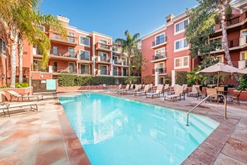 A swimming pool surrounded by lounge chairs and umbrellas in front of a red building.