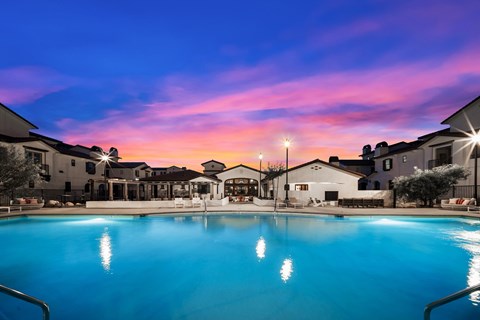 A large swimming pool in front of a building with lights on.