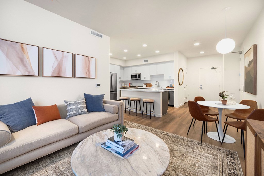 A modern living room with a grey sofa, a round coffee table, and a kitchen in the background at The Villas at Anacapa Canyon, Camarillo, 93012