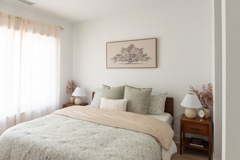 Bedroom with a queen bed, matching nightstands, table lamps, framed artwork, and a large window.