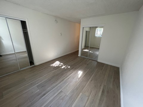 an empty living room with wood flooring and a mirrored closet