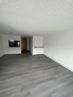 an empty living room with a refrigerator and a microwave