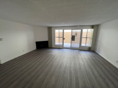 an empty living room with wood floors and a door to a balcony