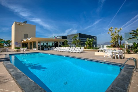 A swimming pool with sun loungers and a building in the background.