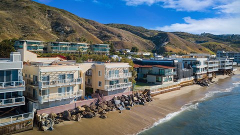 a group of people walking on the beach next to buildings