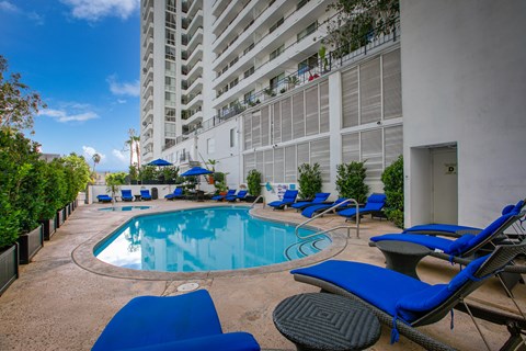 a swimming pool with blue chairs in front of a tall building