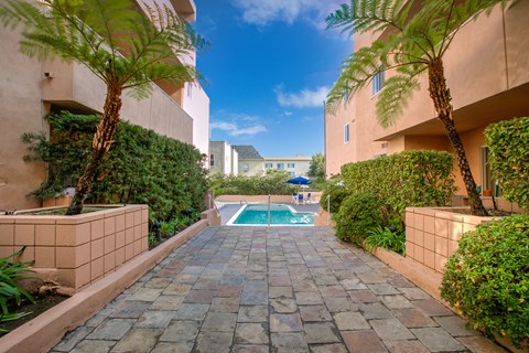 a walkway between two apartments with a pool and palm trees