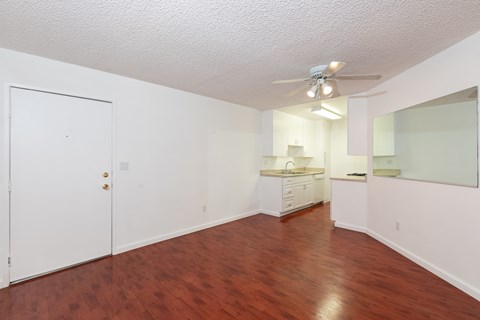 an empty living room and kitchen with wood flooring and a ceiling fan