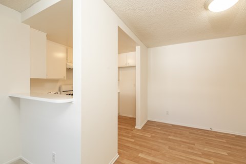 an empty living room and kitchen with wood flooring and white walls