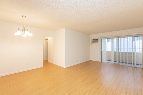 the living room and dining room of an apartment with wood flooring and a window
