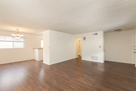 the living room and dining room of an apartment with wood floors and white walls